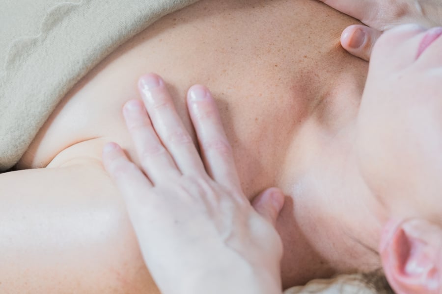 Masseur massaging pleased young woman on massage table in spa salon. Young woman receiving a decollete massage in a spa center. Female patient is receiving treatment by professional therapist.